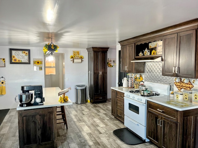 kitchen featuring white range with gas cooktop, light countertops, backsplash, and dark brown cabinetry