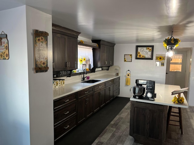 kitchen featuring light countertops, a breakfast bar area, dark brown cabinetry, and a sink