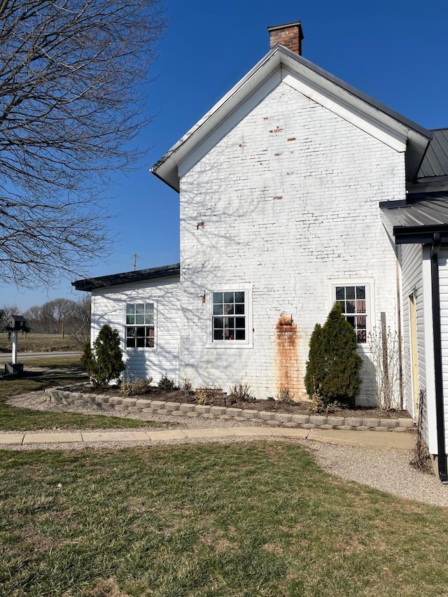 view of property exterior featuring brick siding, metal roof, a lawn, and a chimney