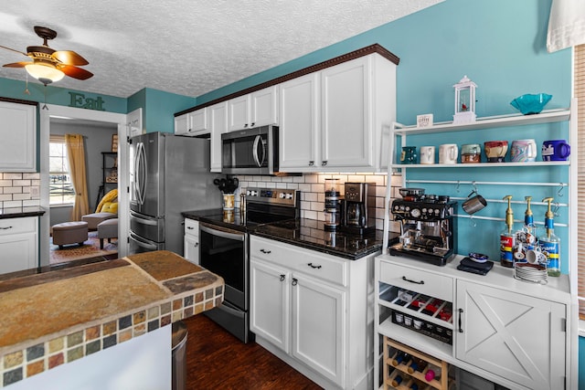 kitchen featuring dark countertops, decorative backsplash, appliances with stainless steel finishes, white cabinetry, and dark wood-style flooring