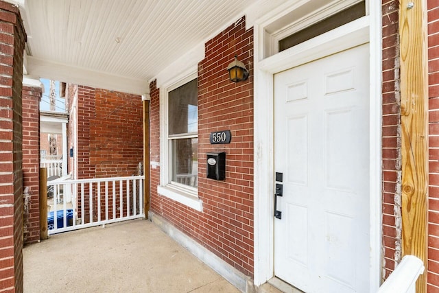 view of exterior entry with a porch and brick siding