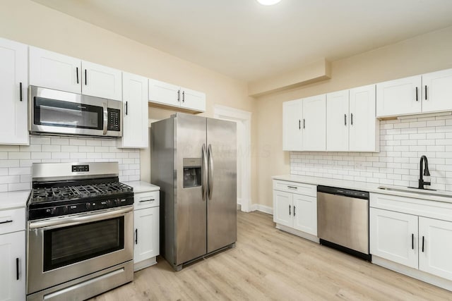 kitchen featuring light wood-type flooring, light countertops, white cabinets, stainless steel appliances, and a sink