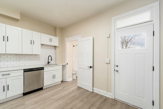 kitchen with light wood finished floors, a sink, light countertops, stainless steel dishwasher, and tasteful backsplash