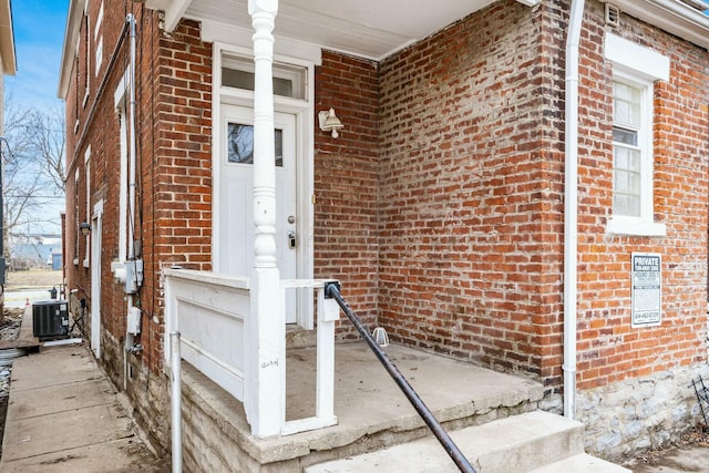 view of exterior entry featuring brick siding and central AC