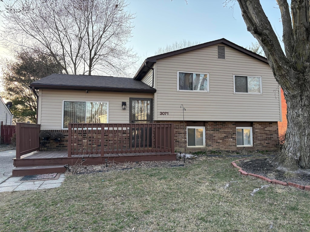 rear view of property with a yard, brick siding, and a wooden deck