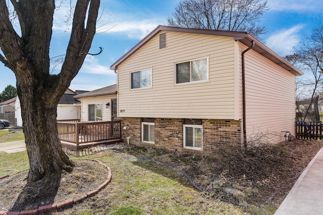 view of side of home with brick siding, a deck, and fence