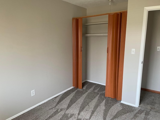 unfurnished bedroom featuring dark colored carpet, a closet, and baseboards