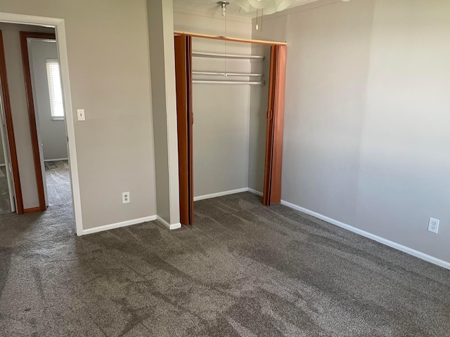 unfurnished bedroom with a closet, baseboards, and dark colored carpet