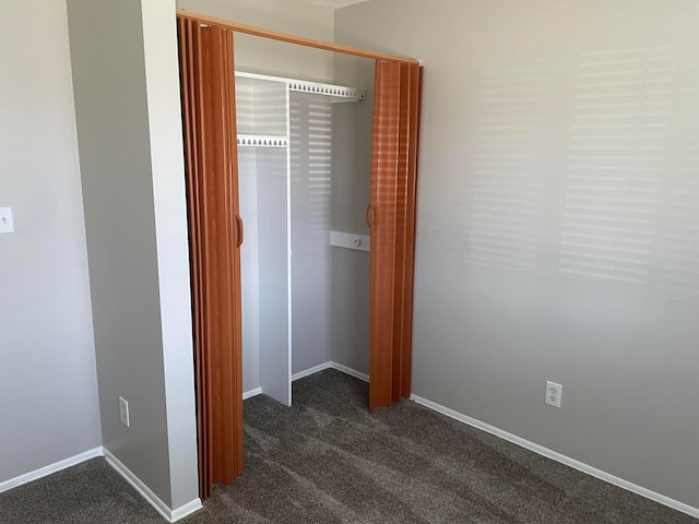 unfurnished bedroom with a closet, baseboards, and dark colored carpet