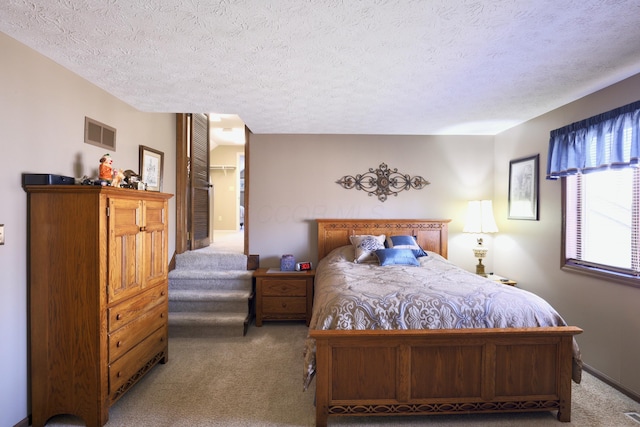 bedroom with a textured ceiling, a spacious closet, visible vents, and light carpet