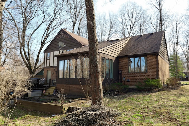 view of side of property with brick siding, a garden, roof with shingles, and a sunroom