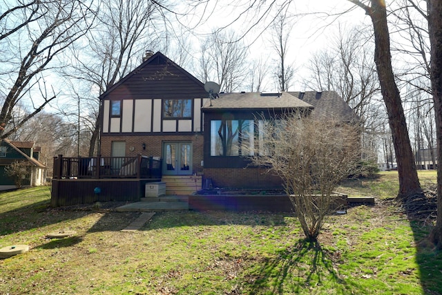 tudor house featuring brick siding, a chimney, a wooden deck, and a front lawn