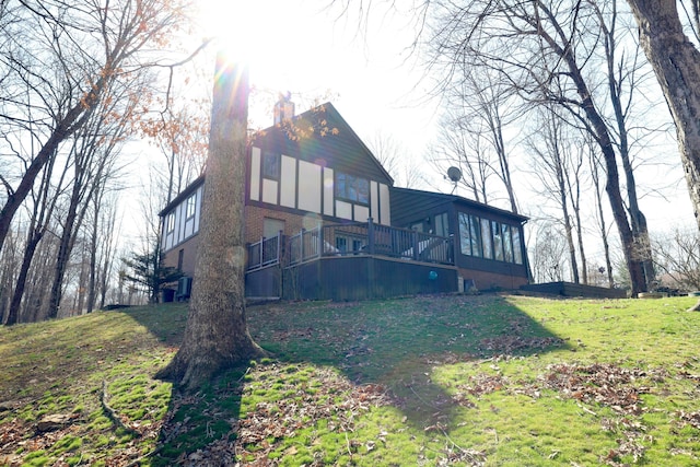 back of house with a yard, brick siding, a wooden deck, and a chimney