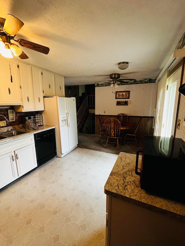 kitchen with wallpapered walls, ceiling fan, black dishwasher, white refrigerator with ice dispenser, and white cabinets