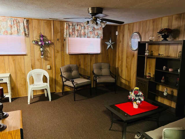 living area with carpet flooring, wooden walls, a textured ceiling, and a ceiling fan