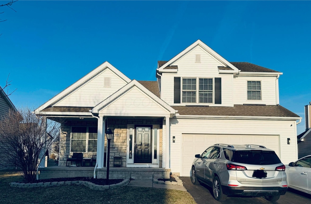 traditional home with driveway, stone siding, roof with shingles, covered porch, and an attached garage