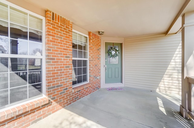 view of exterior entry with a porch and brick siding