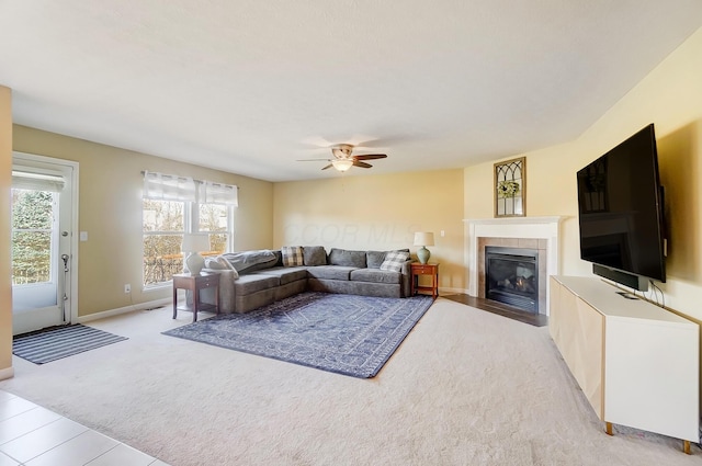 living room featuring baseboards, light carpet, a ceiling fan, and a tiled fireplace