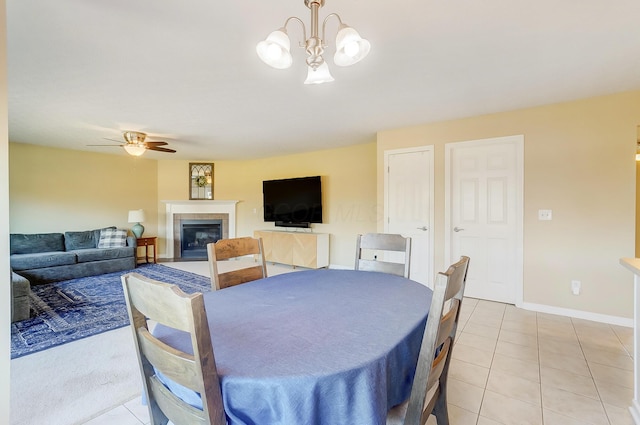 dining space featuring light tile patterned floors, ceiling fan with notable chandelier, baseboards, and a fireplace with flush hearth