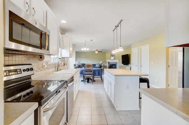 kitchen featuring a sink, stainless steel appliances, white cabinets, a glass covered fireplace, and tasteful backsplash