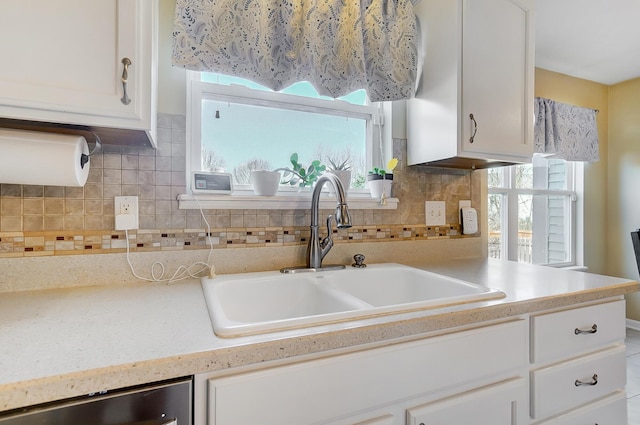 kitchen with a sink, backsplash, stainless steel dishwasher, white cabinets, and light countertops