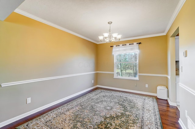 spare room featuring a notable chandelier, ornamental molding, baseboards, and wood finished floors