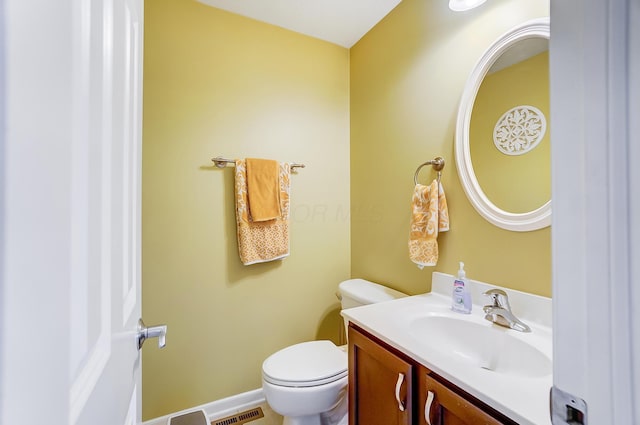 half bathroom with visible vents, toilet, vanity, and baseboards