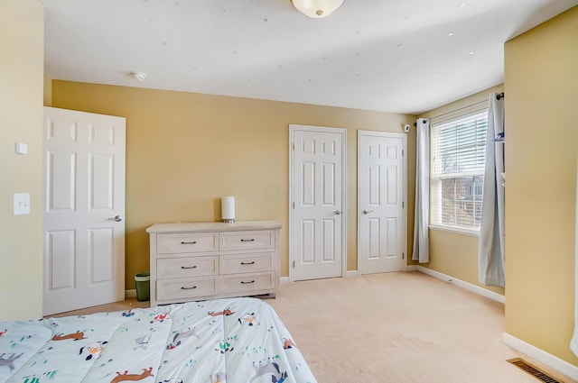 unfurnished bedroom with light carpet, baseboards, visible vents, and multiple closets