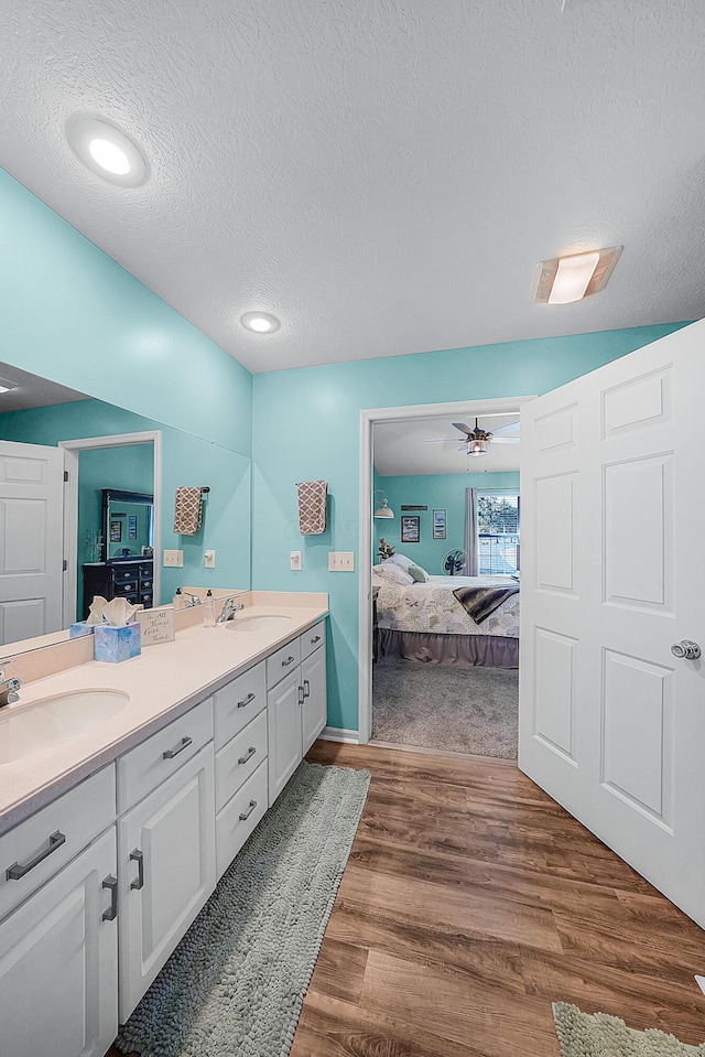 bathroom with ensuite bathroom, a sink, a textured ceiling, wood finished floors, and double vanity