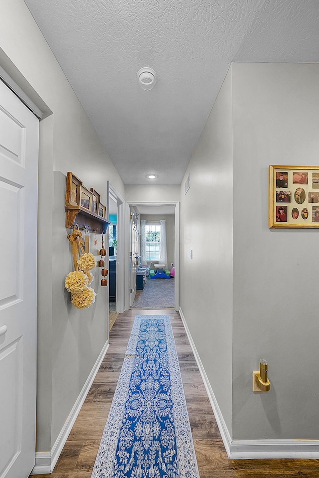 corridor featuring visible vents, wood finished floors, baseboards, and a textured ceiling