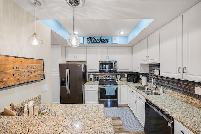 kitchen featuring decorative backsplash, hanging light fixtures, white cabinets, stainless steel appliances, and a sink