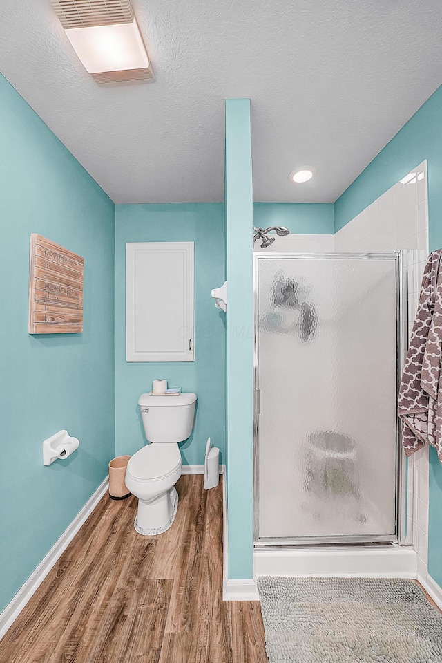 bathroom with wood finished floors, baseboards, a stall shower, a textured ceiling, and toilet