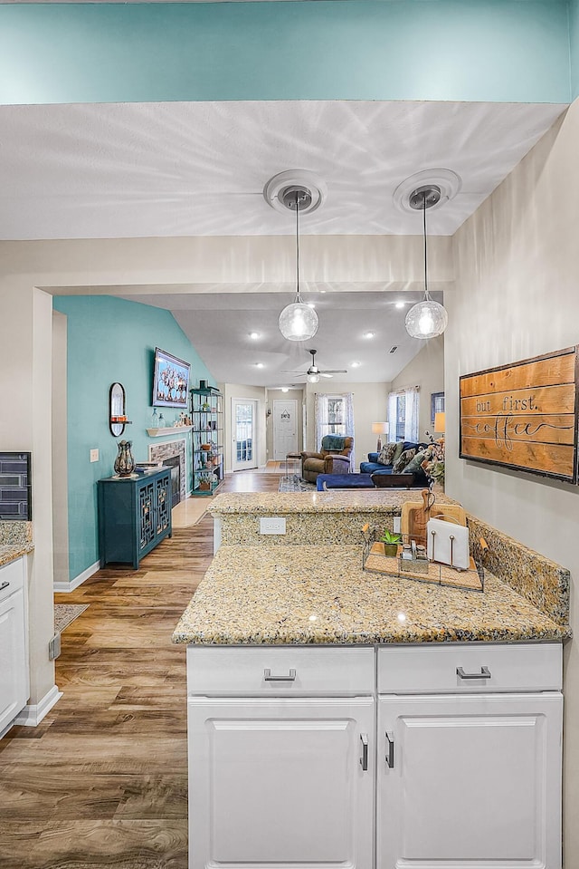 kitchen with open floor plan, vaulted ceiling, a fireplace, wood finished floors, and hanging light fixtures