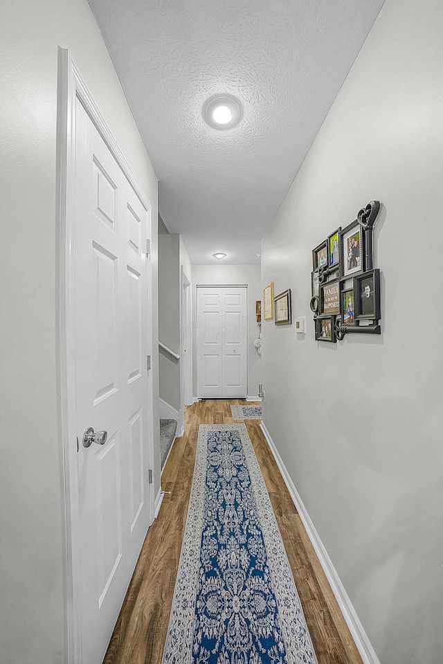 hall featuring a textured ceiling, baseboards, and wood finished floors