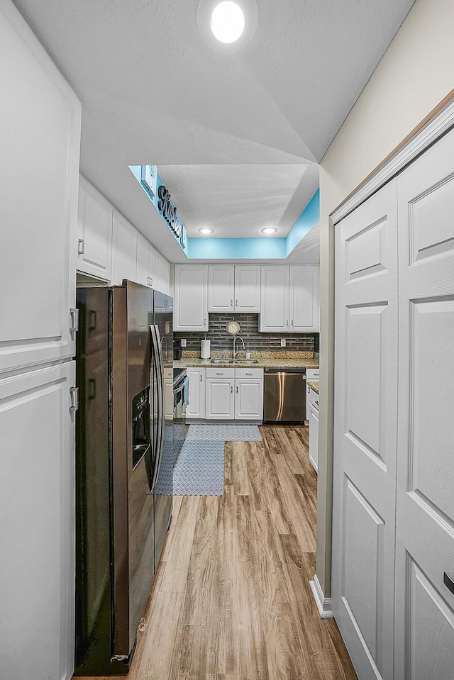 kitchen with light wood-type flooring, a sink, backsplash, stainless steel appliances, and white cabinets