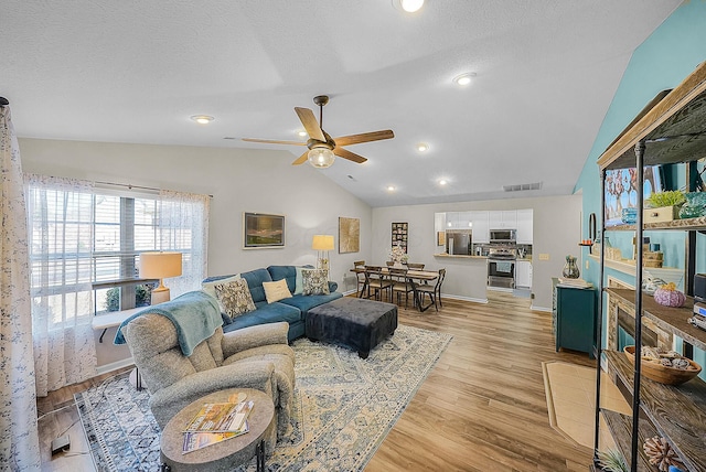 living room featuring a ceiling fan, visible vents, vaulted ceiling, a textured ceiling, and light wood-type flooring