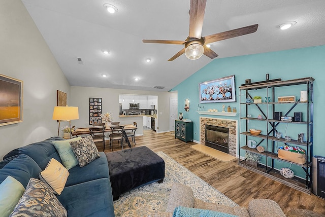 living area featuring a glass covered fireplace, visible vents, lofted ceiling, and wood finished floors