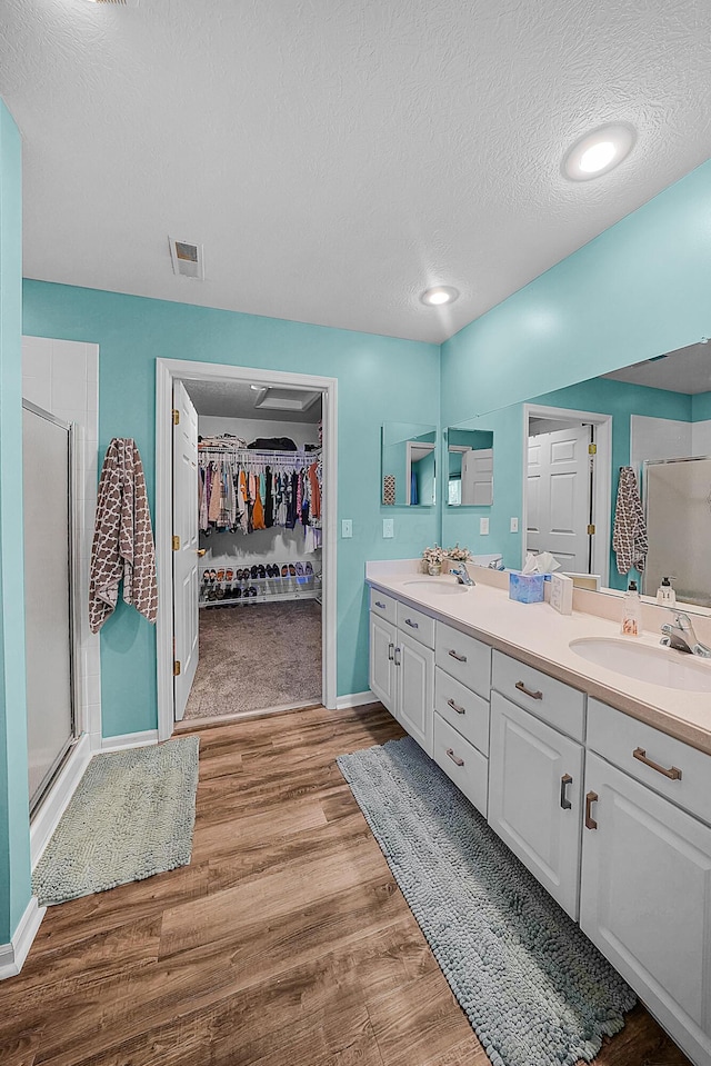 full bath with double vanity, a stall shower, wood finished floors, and a sink