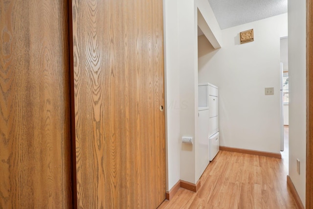 hallway with light wood finished floors, a textured ceiling, and baseboards