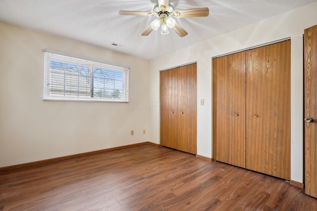 unfurnished bedroom with visible vents, two closets, a textured ceiling, wood finished floors, and baseboards