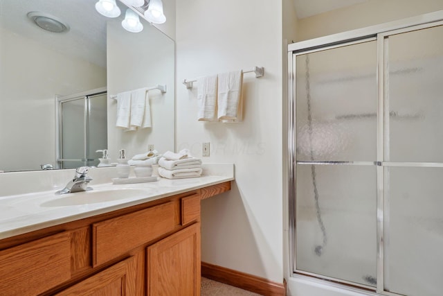 full bath featuring a shower with shower door, baseboards, and vanity