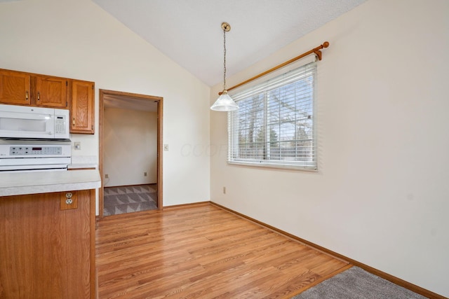 unfurnished dining area featuring baseboards, light wood-style flooring, and vaulted ceiling