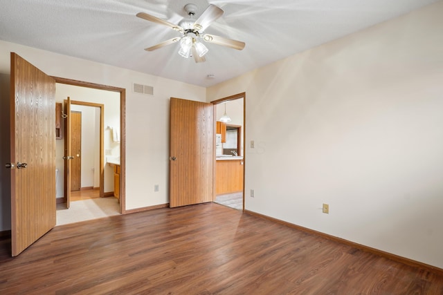 unfurnished bedroom featuring visible vents, ensuite bath, baseboards, and wood finished floors