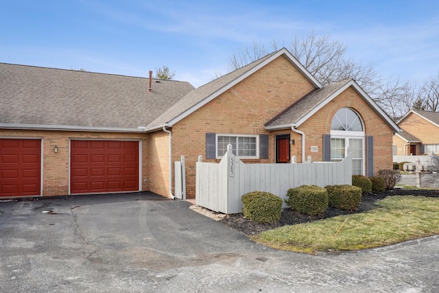 view of front of home featuring a garage, brick siding, a fenced front yard, and a shingled roof