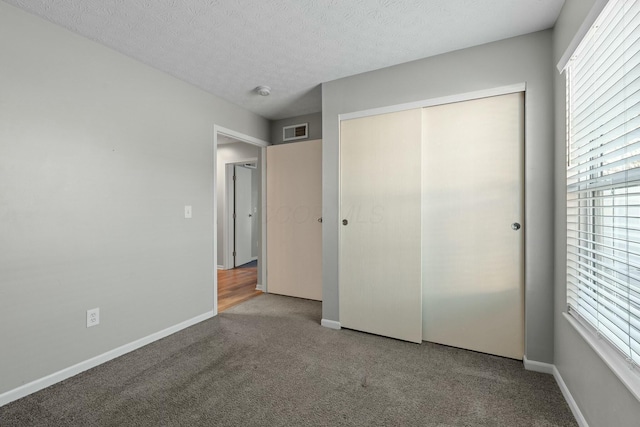 unfurnished bedroom featuring visible vents, baseboards, carpet flooring, a closet, and a textured ceiling