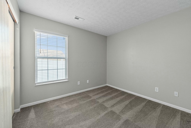 empty room featuring visible vents, carpet flooring, a textured ceiling, and baseboards