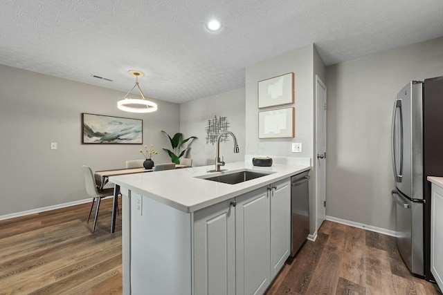 kitchen featuring a sink, light countertops, appliances with stainless steel finishes, a textured ceiling, and dark wood-style flooring