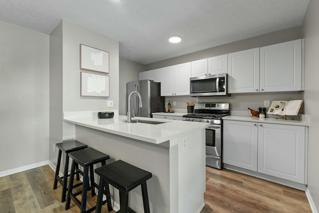 kitchen featuring a breakfast bar area, wood finished floors, a sink, stainless steel appliances, and white cabinets