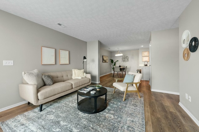 living room with dark wood finished floors, visible vents, a textured ceiling, and baseboards