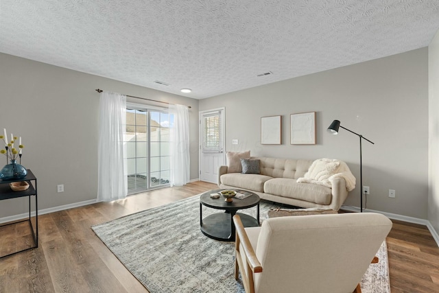 living area featuring visible vents, baseboards, a textured ceiling, and wood finished floors